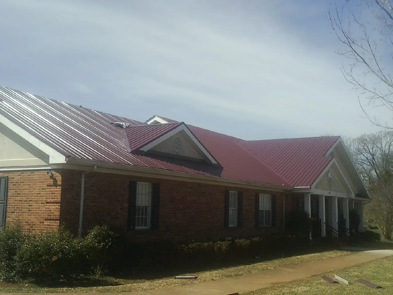 Red metal roof with gabled entries on a long brick building, from a Hail Damage Roof Repair job in Keswick