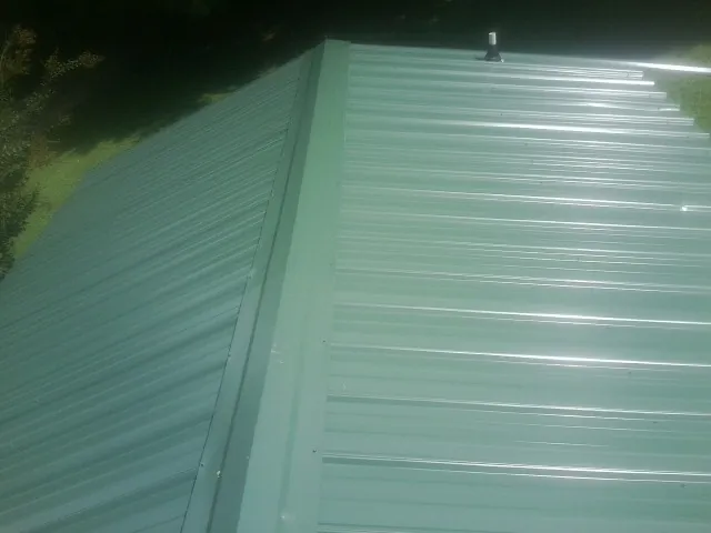 New green metal panels meeting at the ridge of a roof — Flat Roof Repair work by our crew in Keswick