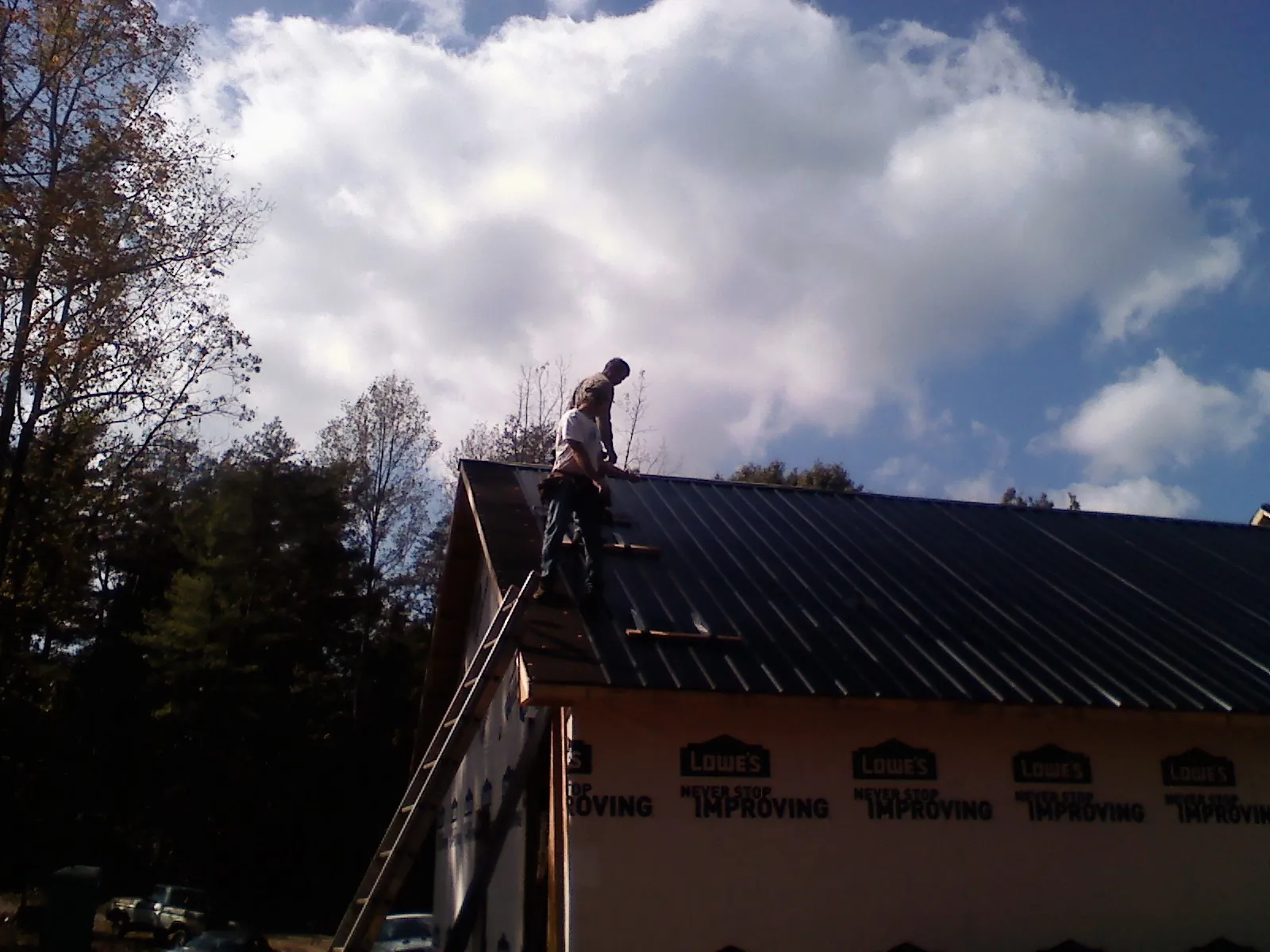 Roofer fastening dark metal panels high against a cloudy sky, from a Roof Inspection job in Keswick