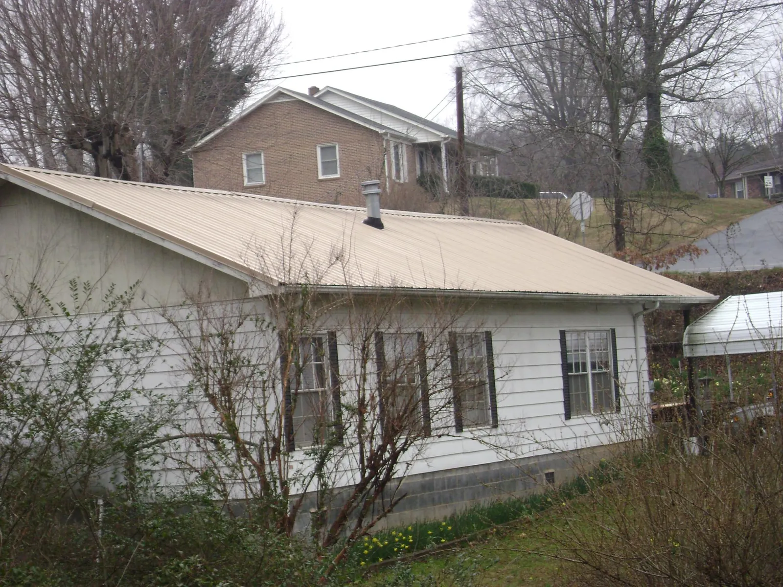 Tan metal roof on a white sided house set into a hillside — Commercial Roofing by Roofing Brothers in Keswick