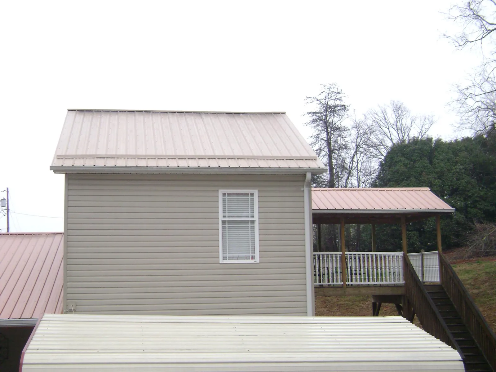Tan metal roofs on a two story addition and attached porch, from a Roof Replacement job in Keswick